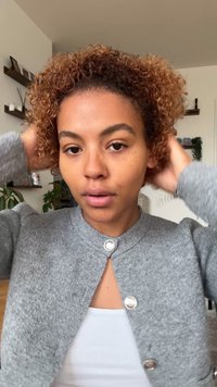 Grå stickad kofta med rund halsringning och knappstängning fram. Kort lockigt hår och naturlig hudton syns.