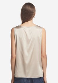 Beige satin ärmlös topp med rund halsringning, slät textur och sidoklipp, visad bakifrån, med långt brunt hår synligt.