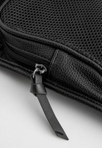 Bolso negro con un exterior de cuero texturizado, panel de malla y cierre de cremallera con una correa en bucle para facilitar su manejo.