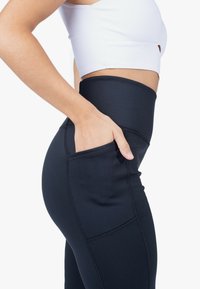 Leggings neri a vita alta con tasca laterale, texture liscia e cuciture a contrasto, design aderente che mette in evidenza la vita e i fianchi.