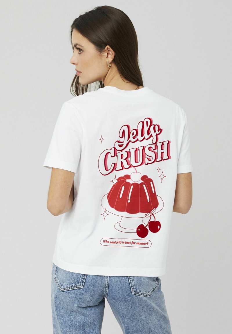 T-shirt en coton blanc avec un graphique coloré "Jelly Crush" représentant un moule à gelée, des cerises et du texte au dos. Manches courtes et coupe décontractée.