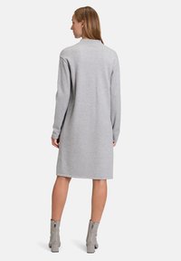 Abito in felpa grigia con maniche lunghe, design sopra il ginocchio, scollatura rotonda e trama uniforme, abbinato a stivali con tacco grigio chiaro.