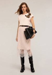 Ljusrosa t-shirt med blommönster, som är kombinerad med en genomskinlig spetskjol, svart bälte och svarta knähöga stövlar. Inkluderar en svart handväska.