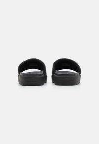 Sorte slip-on sandaler med en tekstureret overdel, glat gummisål og diskret branding på hælen. Åben design uden bagdel.