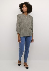 Sort og hvid mønsterbluse med rund hals, lange ærmer, parret med blå denim slim-fit jeans og beige hæle med sorte spidser.