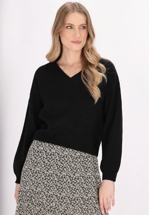 Schwarzer Strickpullover mit V-Ausschnitt und weiten Ärmeln, kombiniert mit einem Rock im Blumendesign in dunklen Farben und kleinen weißen Blumen.