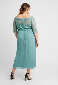 Teal kvällsklänning med spetsöverdrag på bodicen och trekvartslånga ärmar. Flödande material, insydd midja och ankellång nederdel. Svarta klackskor.