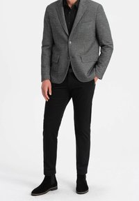 Szara teksturowana marynarka z wyciętymi klapami, czarna koszula pod spodem, wąskie czarne spodnie oraz czarne botki zamszowe na jasnej podeszwie.