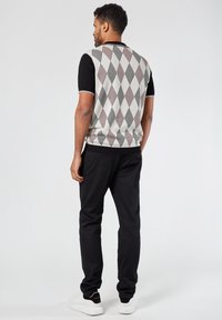 Knit short-sleeve sweater in cream with black and maroon diamond pattern; paired with black pants and white sneakers.