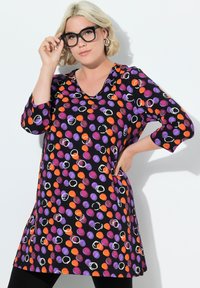 Schwarze Tunika mit mehrfarbigen Punkten in Lila, Orange und Weiß. Mit V-Ausschnitt und Dreiviertelärmeln. Glenzender Stoff.