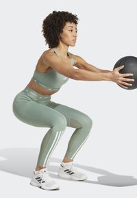 Conjunto deportivo en verde claro; sujetador deportivo y leggings de tiro alto con paneles y franjas blancas. Tejido compresor, posición de sentadilla enfocada.