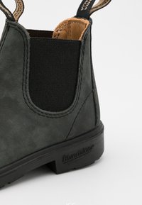 Bota Chelsea de cuero negro con paneles laterales elásticos, costuras en contraste y una suela de goma con el logo "Blundstone" en el talón.