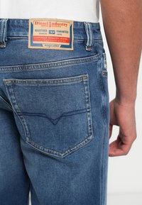 Modré denimové džínsy majú vybledlý vzhľad, rovný strih a zadné vrecko s kontrastným prešitím. Vidieť je aj kožená nášivka s logom značky.