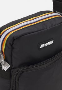 Schwarze Nylon-Tasche mit mehreren Reißverschlussfächern, die oben einen bunten Streifenakzent in Grün, Weiß, Orange und Blau aufweist. K-WAY-Logo sichtbar.