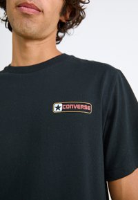 Sort bomulds t-shirt med et farvet "Converse" logo patch med en hvid stjerne. Korte ærmer og rund halsudskæring. Blød tekstur.
