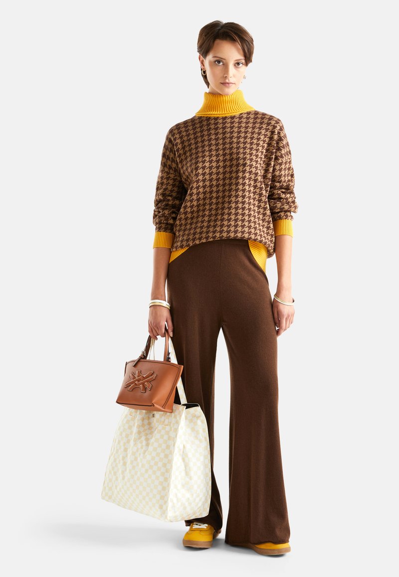 Brązowy sweter w wzór houndstooth z żółtym golfem, beżowe spodnie typu wide-leg oraz brązowa torebka. Obecna jest również żółta torebka w kratkę.