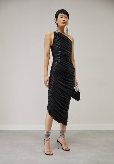 Schwarzes, einseitiges Kleid mit geraffter Textur, knielang. Kombiniert mit silbernen, mehrsträngigen Knöchelarmbändern und High-Heels.