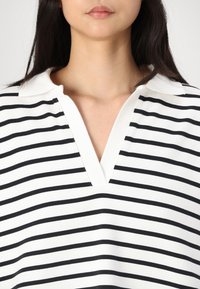 Stripet topp med svarte og hvite horisontale striper, krage og V-hals design. Myk stoff med en jevn tekstur.