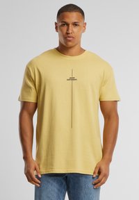 Camiseta de algodón amarilla con mangas cortas, que presenta un texto impreso en negro "PIENSA DIFERENTE." centrado verticalmente en la parte delantera.