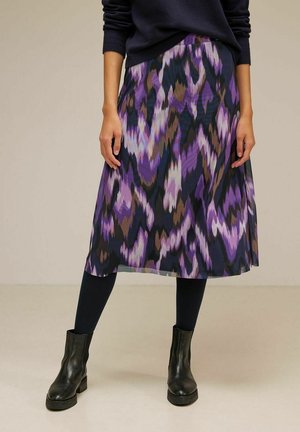 Falda de longitud media con un patrón abstracto en tonos morado, negro y marrón, combinada con medias negras, botas negras y un suéter oscuro.