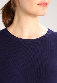 Haut en tricot côtelé bleu marine avec un col rond. La texture est finement côtelée, mettant en avant un design ajusté sans aucun matériel ou accent visible.