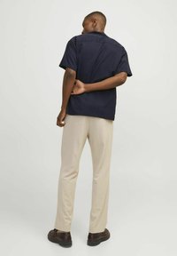 Short-sleeve navy shirt with a straight cut, paired with beige trousers and dark shoes. The shirt features a simple collar and back seam details.