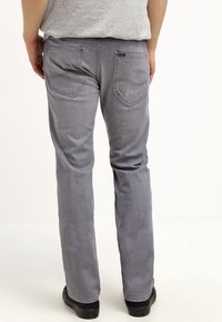 Jeans rectos grises con una textura desgastada, que cuentan con dos bolsillos traseros y detalles de costura visibles, combinados con zapatos negros.