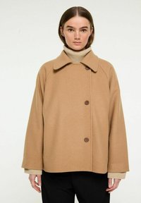 Brun uldmix frakke med en bred krave, to knapper og raglanærmer, parret med en lys beige turtleneck under.