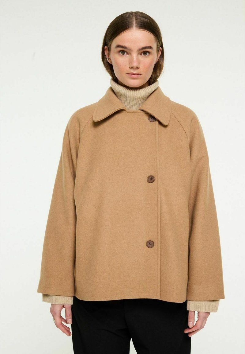 Brun uldmix frakke med en bred krave, to knapper og raglanærmer, parret med en lys beige turtleneck under.