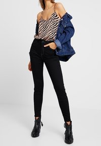 Svarta tight jeans i kombination med en zebrarandig satin camisole och en blå denimjacka. Utrustad med axelremmar, en figurnära design och ankelstövlar.