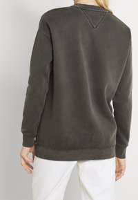 Tmavě šedá mikina s uvolněným střihom, žebrovanými manžetami a lemem. Disponuje výstřihem do V a měkkou, strukturovanou tkaninou.
