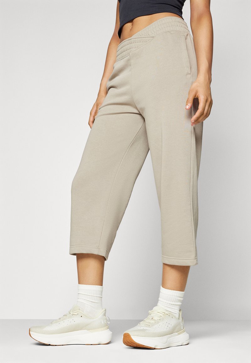 Beige, kurze Sweatpants aus weichem Stoff, mit einem elastischen Bund und seitlichen Taschen, kombiniert mit hellen Sneakers und weißen Socken.