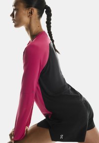 Atletska odjeća s dugim ružičastim rukavima i crnim tijelom, koja ima prozračnu teksturu i logo na kratkim hlačama. Elegantno, prilagođeno dizajn.