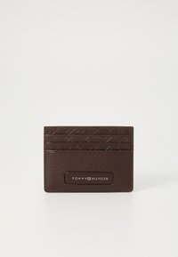 Brun lærveske med teksturert design, flere kortlommer og en rektangulær etikett med 'TOMMY HILFIGER' i hvitt.