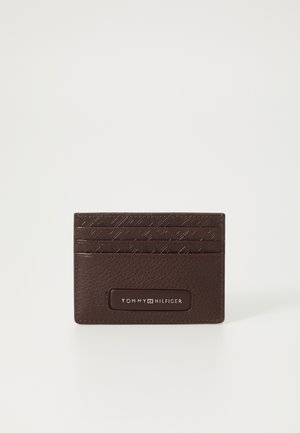 Pruun nahast kaarditasku, millel on tekstuuriga disain, mitu kaardipesa ja ristkülikukujuline silt, millel on valgete tähtedega 'TOMMY HILFIGER'.
