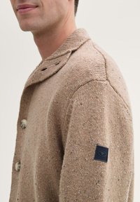 Beige Wolle-Mix Pullover mit einem gerippten Kragen, großen Knöpfen und einer strukturierten Oberfläche, mit einem schwarzen Logo-Patch an den Ärmeln.
