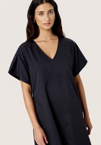Black cotton dress with a V-neck, short wide sleeves, and a seam detail on the front, featuring a relaxed, loose silhouette.