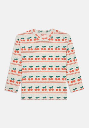 Chemise beige à manches longues avec un motif de cerises répétées en rouge et vert, étiquetée "TINY" à l'intérieur du col.
