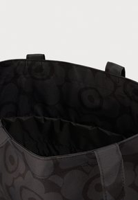 Μαύρη τσάντα tote με σκούρο λουλουδάτο σχέδιο, δύο λαβές και ανοιχτό πάνω μέρος που δείχνει την εσωτερική επένδυση.