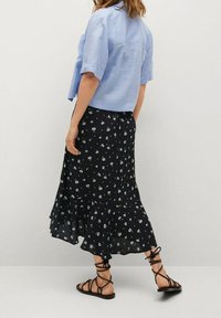 Camicetta corta azzurro chiaro con maniche arrotolate abbinata a una gonna nera con stampa floreale, caratterizzata da un orlo ondulato e sandali neri con strappi.