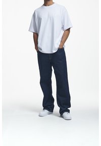 Bílá oversized tričko v kombinaci s tmavě modrými volně střiženými džíny. Bílé tenisky celý outfit doplňují. Jednoduchý design, ležérní styl.