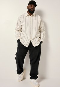 Camisa de botones en crema con rayas verticales negras, combinada con pantalones anchos negros y zapatillas blancas. Presenta un bolsillo en el pecho y un cuello.