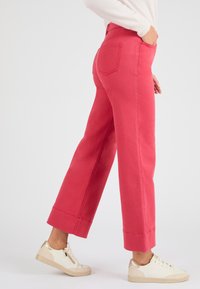 Pantalones rosa de talle alto y pernera ancha en tejido de algodón, con dobladillo limpio y bolsillos traseros, combinados con zapatillas blancas y doradas.
