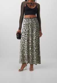 Černý crop top s třpytivými dlouhými rukávy, spárovaný s volnou maxi sukni s černobílým květinovým vzorem. Průhledné sandály na podpatku.