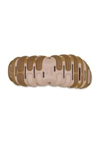 De schoen heeft een dikke, golvende zool in beige met bruine accenten, gemaakt van zacht materiaal, en bevat ventilatieopeningen voor ademend vermogen.