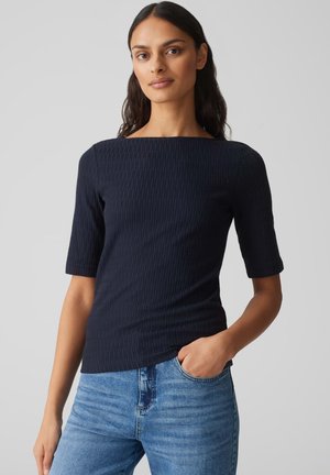 Navy ribbed short-sleeve top with a square neckline, paired with light blue denim jeans. Smooth texture and fitted design.