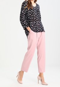 Schwarze Bluse mit buntem Blumenmuster, kombiniert mit hellrosa, tapered Hosen und nude-farbenen High Heels. Lockere Passform und leichtes Material.