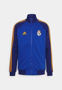 Blå zip-up jacka med orange detaljer, med Adidas-logotypen och Real Madrid-emblemet, tillverkad av mjukt tyg, med ribbade muddar och krage.