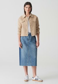Beige wollen blend jas met voorzakken en knoopsluiting, gecombineerd met een lichtblauwe denimrok met een middennaad en rafelige zoom. Witte sneakers.