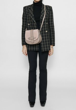 Sac bandoulière beige de forme arrondie, avec des bords noirs contrastants et un détail matériel central. Matériau texturé avec des accents lisses.